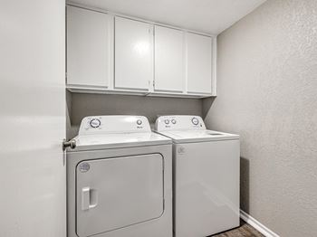 A washer and dryer in an empty laundry room with white cabinets